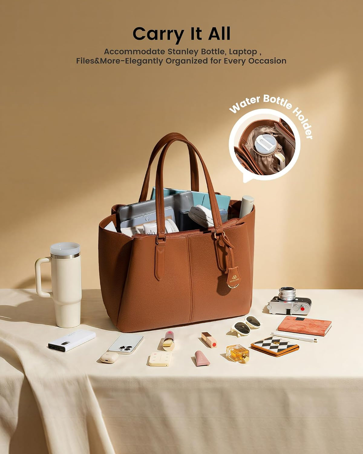 The tote packed on a table beside a tall tumbler, a camera, sunglasses and a notebook